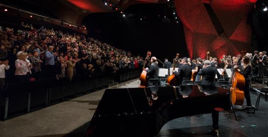 Orkiestra stoi na scenie, po lewej stronie publiczność bije brawo