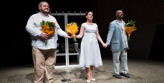Troje solistów stoi na scenie z kwiatami, w środku kobieta a po bokach mężczyźni