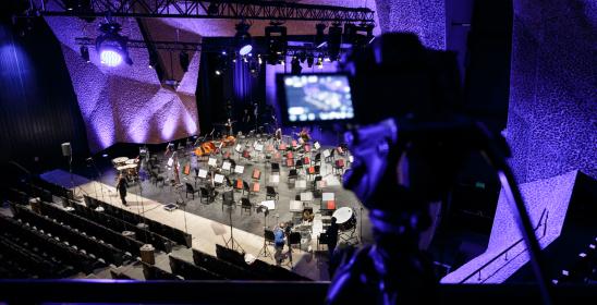 Pulpity na scenie sali koncertowej oraz ustawiona kamera do nagrania koncertu