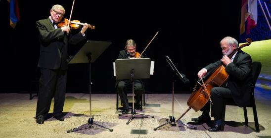 Trzech mężczyzn gra w trio skrzypcowym na scenie w sali kameralnej