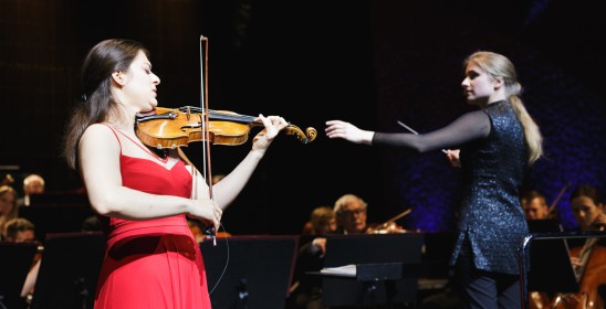 kobieta grająca na skrzypcach i dyrygentka z uniesionymi rękoma