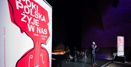 roll-up projektu Póki Polska żyje w nas i mężczyzna mówiący do mikrofonu