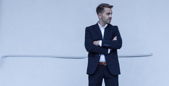 mężczyzna w ciemnym garniturze stojący na jasnym tle