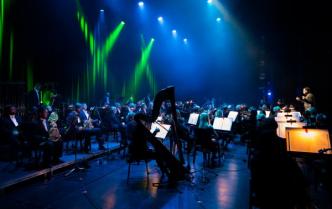 zdjęcie zrobione z boku sceny w kolorach niebieskiego oświetlenia siedzą muzycy orkiestry symfonicznej