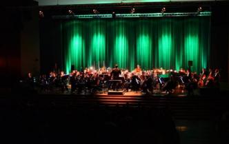 orkiestra siedzi na scenie i gra, tło podświetlone na zielono