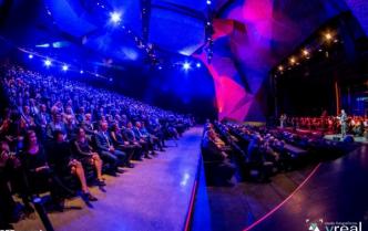 publiczność zgromadzona na sali CKK Jordanki, na scenie orkiestra, wszyscy w niebiesko-fioletowym świetle
