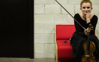 kobietaw czrnej sukni siedzi na czerwonej kanapie trzymając przed sobą skrzypce obok drzwi do garderoby