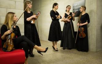 przed wejściem na salę koncertową w czarnych strojach ze skrzypcami w dłoniach czeka  pięć kobiet 