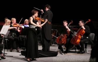 kobieta gra na skrzypcach w tle orkiestra z dyrygentem
