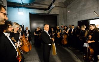 stojący muzycy z instrumentami i dyrygent Dainius Pavilionis w korytarzy przed wejściem na scenę