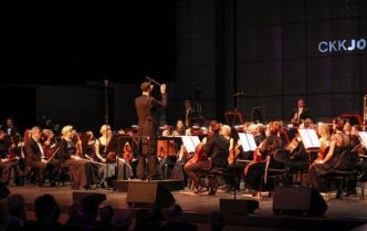 dyrygent z uniesioną batutą stoi przed orkiestrą
