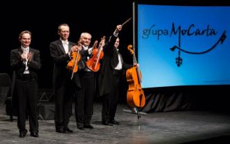 na scenie stoją czterej mężczyźni we frakach z instrumentami smyczkowymi w dłoniach, z boku stoi baner z napisem Grupa Mocatra