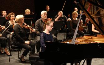 uczennica Zespołu Szkół Muzycznych Karolina Sekuła gra na fortepianie za nią siedzą muzycy trzymając w rękach skrzypce i smyczki