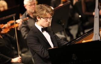 uczeń Zespołu Szkół Muzycznych Stanisław Oracz gra na fortepianie za nim skrzypce w rękach skrzypaczki i siedzący mężczyzna