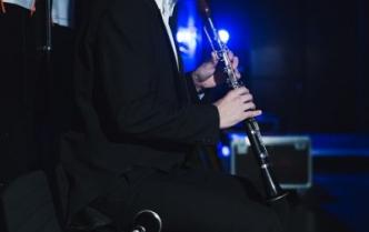 mężczyzna w czarnym garniturze siedząc gra na klarnecie