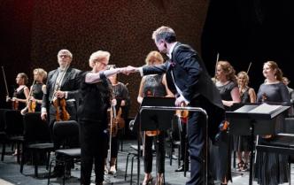 na scenie pochylony mężczyzna dyrygent przybija żółwika z Panią koncertmistrz za nimi stoją muzycy trzymając instrumenty smyczkowe
