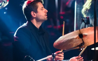 mężczyzna ze skupioną twarzą gra na zestawie perkusyjnym