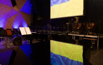 scena Sali Koncertowej CKK Jordanki przygotowana do wystąpienia orkiestry w tle flaga Ukrainy i jej odbicie w fortepianie