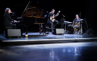 Trzech mężczyzn na scenie grających na fortepianie, gitarze i zestawie perkusyjnym