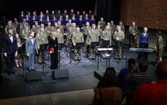 orkiestra wojskowa z chórem i solistami stoi na scenie