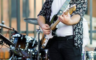 mężczyzna w ciemnych spodniach, białej koszulce i biało-czarnej koszuli grający na gitarze