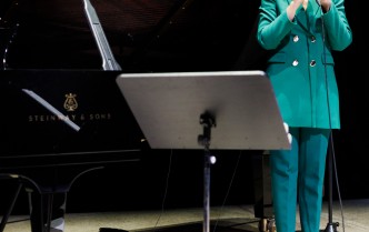 kobieta w zielonym garniturze trzymając w dłoniach mikrofon śpiewa