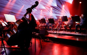 ukazanie kontrabasu i muzyków orkiestry na scenie podczas koncertu w czerwonym i jasnym promienistym oświetleniu