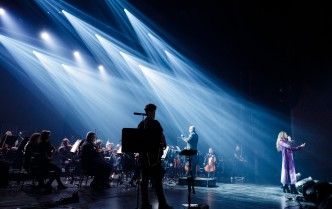 muzycy i wokalista ukazani na scenie na ciemnym tle z punktowym jasnym, zimnym tłem