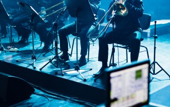 muzycy orkiestry grający na puzonach na scenie, w dolnym prawym rogu zdjęcia fragment sprzętu reżyserii dźwięku