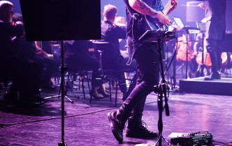 mężczyzna grający na gitarze, stoi na scenie w fioletowym tle