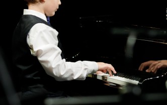 chłopiec w białej koszuli i czarnej kamizelce ukazany bokiem gra na fortepianie