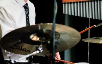 zbliżenie na mężczyznę w białej koszuli i czarnym krawacie grającego na zestawie perkusyjnym