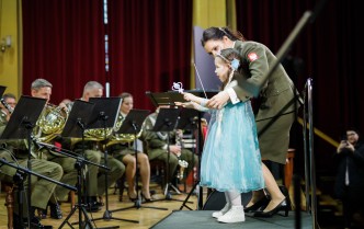 dziewczynka w stroju księżniczki stojąca z dyrygentką przed orkiestrą