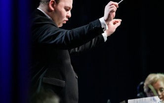 dyrygent z uniesionymi dłońmi podczas dyrygowania orkiestrą
