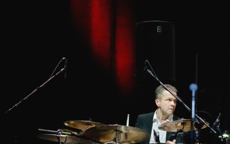 mężczyzna grający na zestawie perkusyjnym na ciemnoczerwonym tle