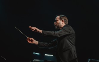 mężczyzna w czarnym garniturze dyrygując orkiestrą