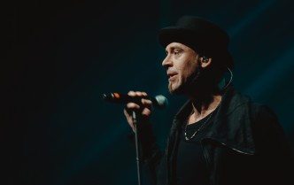 zbliżenie na mężczyznę w ciemnym stroju i kapeluszu śpiewającego do mikrofonu