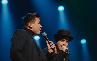 dwaj mężczyźni ubrani w ciemne stroje śpiewający do mikrofonu
