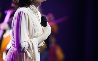 wokalistka stojąca w białej sukni z mikrofonem w dłoni przy piersi
