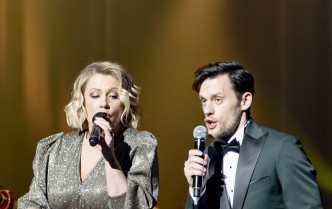 kobieta w złoto-cekinowej sukience i mężczyzna w garniturze wspólnie śpiewają