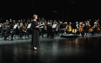 kobieta mówiąca do mikrofonu, w tle siedzi orkiestra