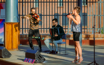 mężczyzna grający na skrzypcach, mężczyzna grający na akordeonie i kobieta śpiewająca do mikrofonu