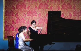 dwie kobiety grające na fortepianie i kobieta stojąca przy fortepianie