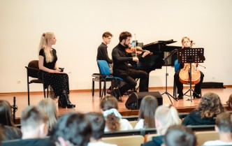 grupa muzyków oraz prowadząca, wszyscy znajdują się na scenie, w dolnej części fotografii widać widownię słuchającą koncertu