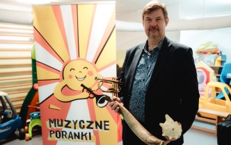 mężczyzna trzymający instrumenty dęte stojący przy rollupie z grafiką projektu