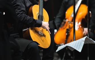 mężczyzna grający na gitarze, za nim w tle mężczyzna trzymający wiolonczelę