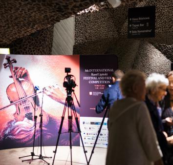 Kamera ustawiona na ściankę promocyjną z grafiką kobiety, która gra na skrzypcach