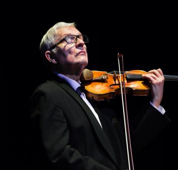 Mężczyzna w okularach w czarnym fraku grający na skrzypcach na czarnym tle