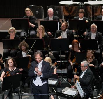 Orkiestra siedzi na scenie a przed nią stoi dyrygent