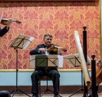 Skrzypek siedzi na krześle na scenie i gra